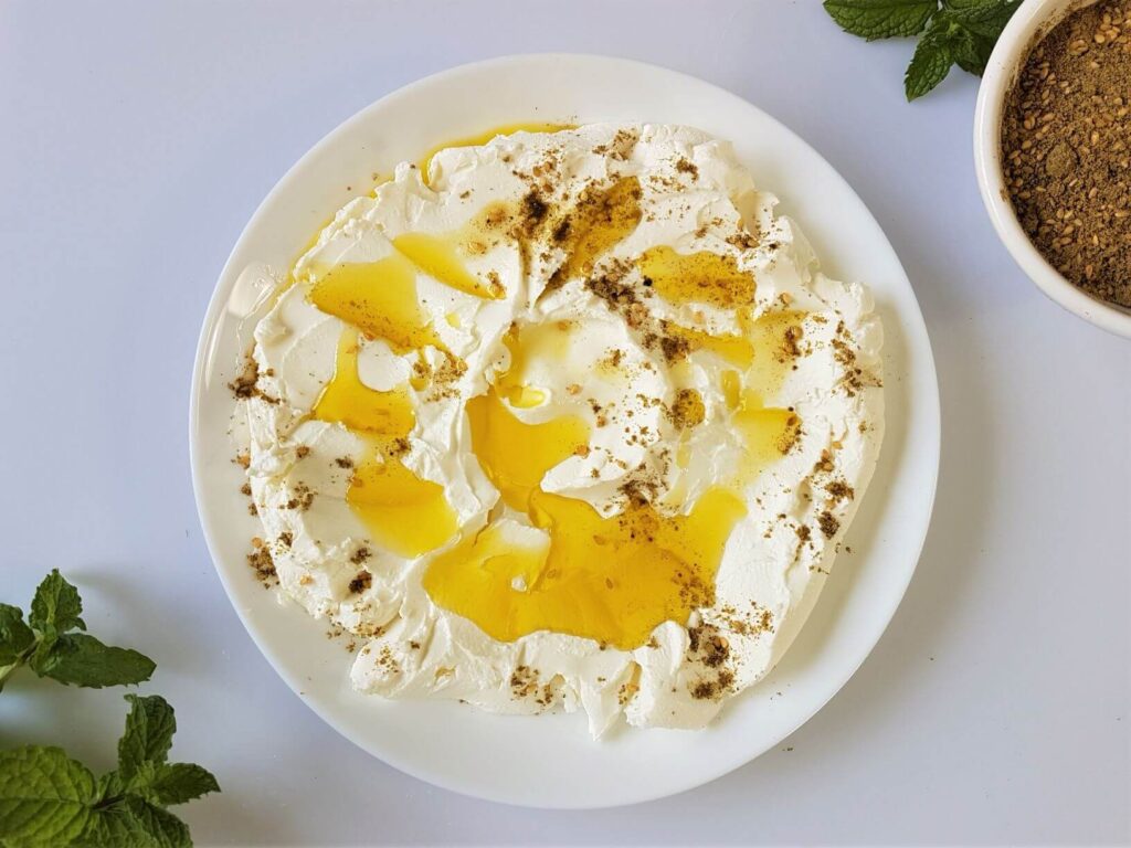 labneh spread on a white plate, topped with olive oil and Zaatar, on white background.