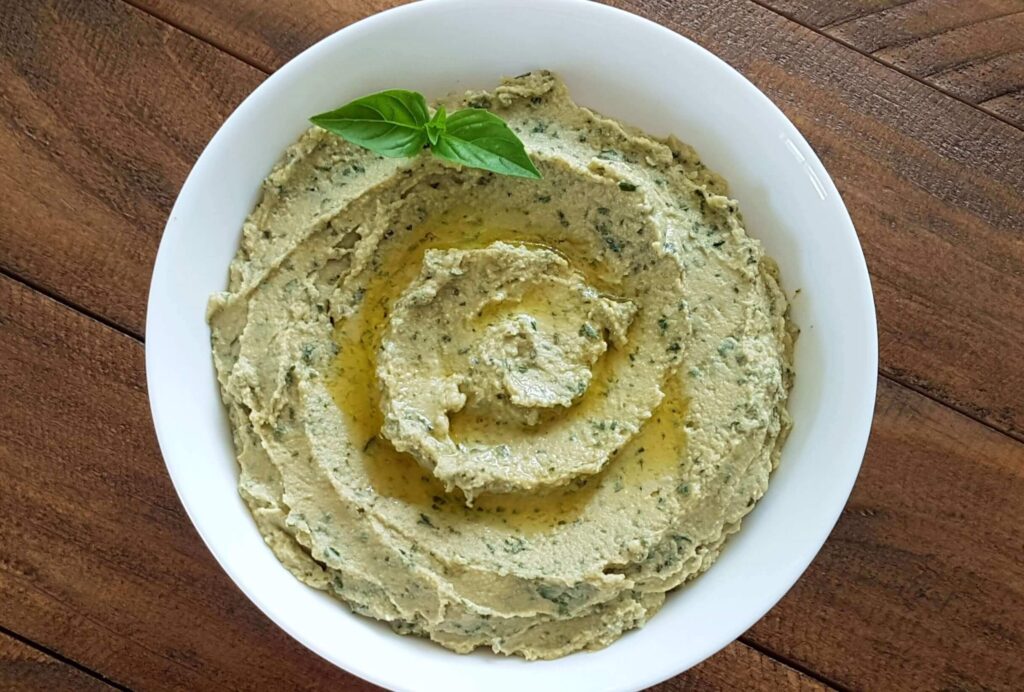 A plate of basil hummus garnished with basil leaves and drizzled with olive oil