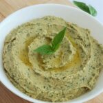 a dish of basil hummus with a drizzle of olive oil, and garnished with basil leaves